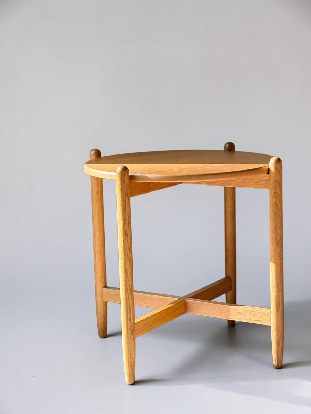 Rundt dansk vintage sidebord i massiv brun eg med skulpturelt krydsstel